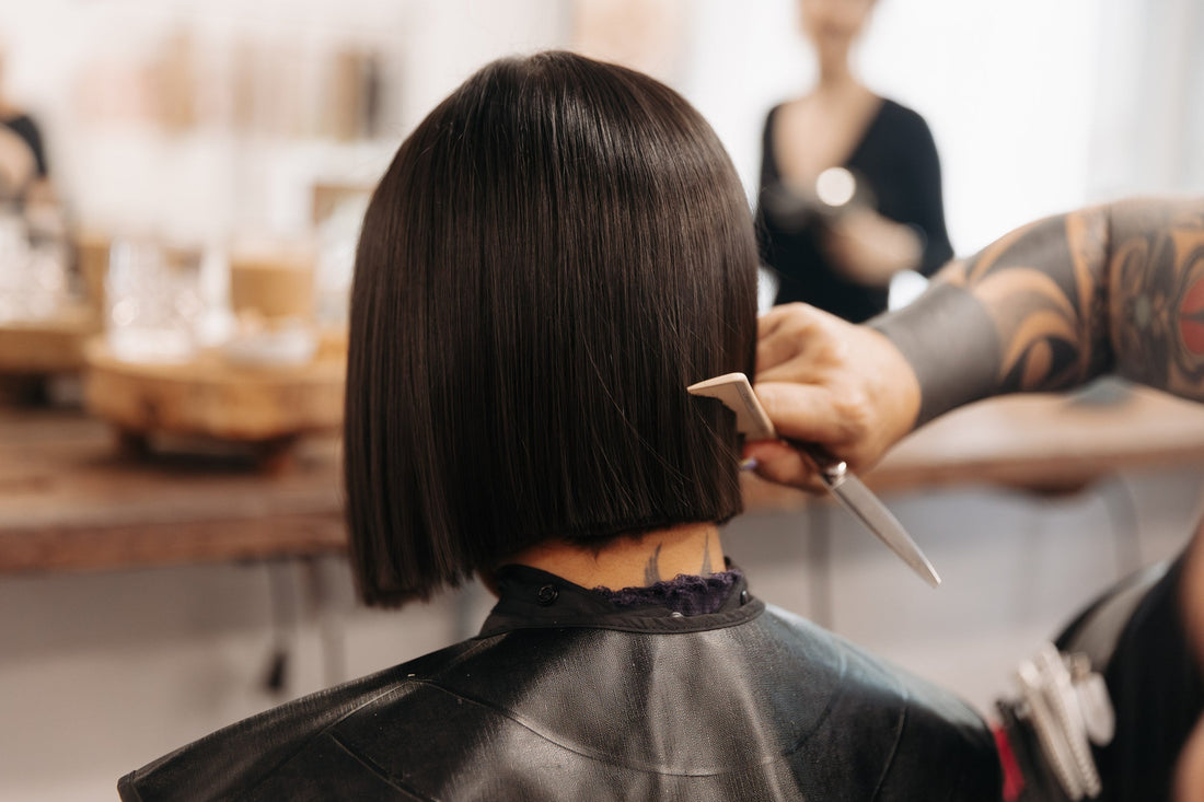 A woman with a short, dark brunette bob getting her hair cut. 