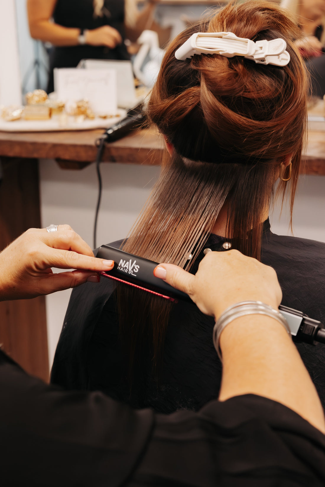 A woman is at the hairdresser and has her hair clipped up, while some of it is being straightened.